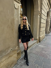 a lady wears a black tweed jacket with a matching shorts and knee high boots